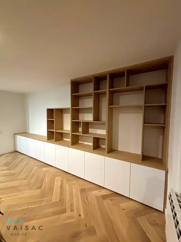Librería a medida en roble sobre muebles bajos blancos en un salón con suelo de espiga